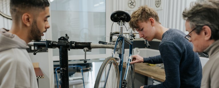 Drei Personen arbeiten gemeinsam an der Reparatur eines Fahrrads in einer Werkstatt.
