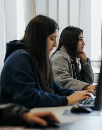 Drei Frauen arbeiten an Desktop-Computern in einem Klassenzimmer, konzentriert auf ihre Bildschirme.