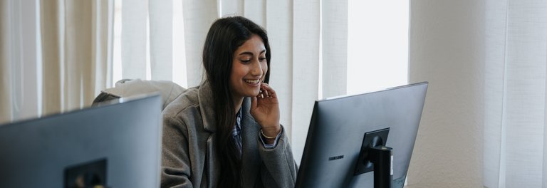 Eine Frau lächelt, während sie in einem hellen, modernen Büro an einem Computer arbeitet.