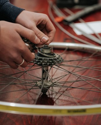Hände reparieren ein Fahrradradgetriebe auf einem Holztisch mit Werkzeugen im Hintergrund.