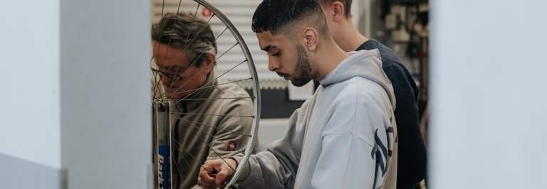 Drei Personen reparieren gemeinsam ein Fahrradrad in einer Werkstatt.