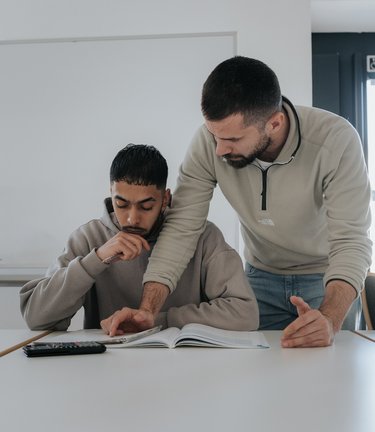 Ein Lehrer hilft einem Schüler bei seiner Arbeit an einem Schreibtisch in einem Klassenzimmer.