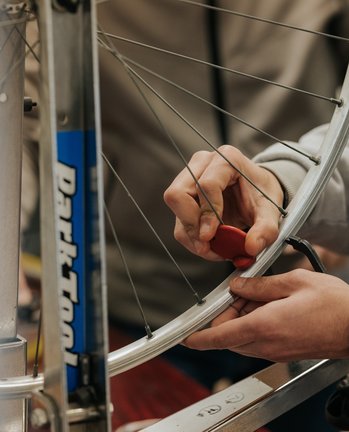 Person, die in einer Werkstatt die Speichen eines Fahrradrades mit einem Speichenschlüssel einstellt.