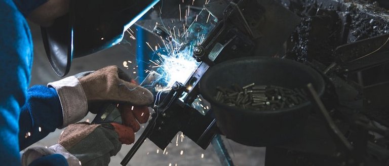 Eine Person mit Schutzausrüstung schweißt in einer Werkstatt Metall mit hellen Funken.