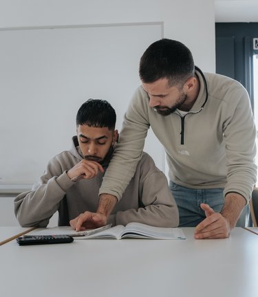 Ein Lehrer hilft einem Schüler bei seiner Arbeit an einem Schreibtisch in einem Klassenzimmer.