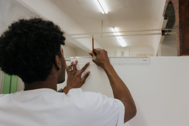 Person, die mit einem Lineal und einem Bleistift eine weiße Fläche in einem gut beleuchteten Raum abmisst und markiert.