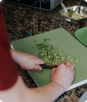 Eine Person schneidet grüne Zwiebeln auf einem grünen Schneidebrett in einer Küche.