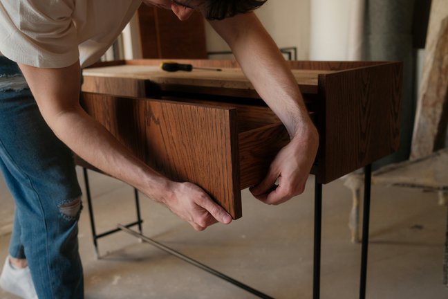 Person, die eine Holzschublade in einem Schrank zusammenbaut, in Jeans und hellem Hemd, in einem Haus.