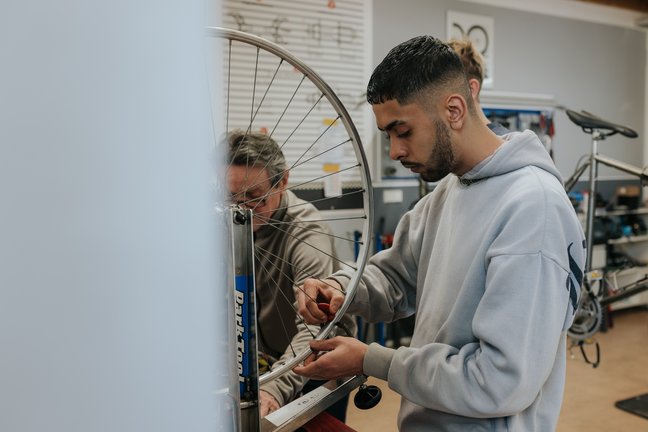 Zwei Personen arbeiten zusammen, um ein Fahrradrad in einer Werkstatt zu reparieren.