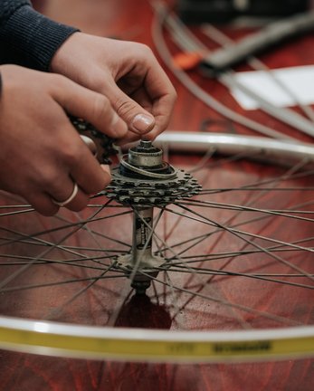 Hände reparieren eine Fahrradnabe und eine Gangschaltung auf einer Holzfläche.